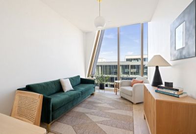 Bright lounge featuring a green velvet sofa, patterned rug, and floor-to-ceiling windows with city views.