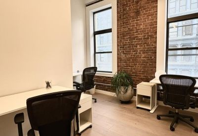 Private office featuring two desks, ergonomic chairs, and a large window against a brick accent wall.