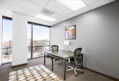 Bright private office with corner windows and a patterned area rug.