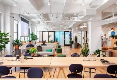 Open-plan coworking office with long wooden tables and various breakout seating areas.