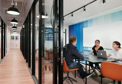 Glass-walled meeting room with three people collaborating at a table with laptops.