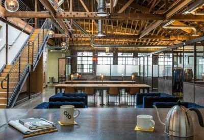 Industrial-style coworking space with long wooden tables and exposed ceiling beams.