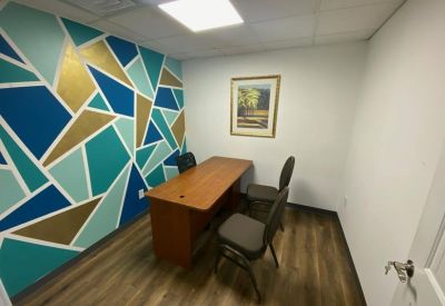 Bright private office featuring a vibrant teal and gold geometric accent wall and wooden desk.