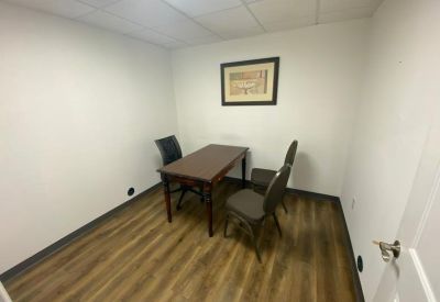 Small meeting room with a simple wooden table and two grey chairs against white walls.