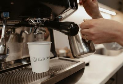 Close-up of a coffee machine pouring into a branded paper cup in a bright kitchen area.