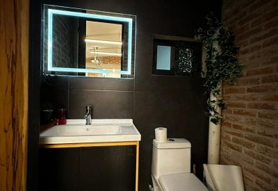 Sleek restroom featuring dark tiles, an LED-backlit mirror, and brick accents.