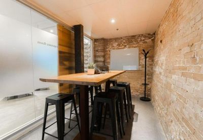 High-top meeting table with black stools against an exposed brick wall and whiteboard.