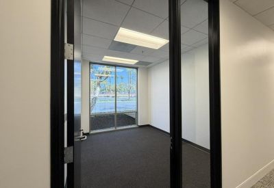 Unfurnished office space with a large window and dark carpeting viewed through glass doors.