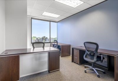Private office featuring dark wood desks, ergonomic chairs, and a window view.