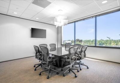 Modern conference room with a glass table, mesh chairs, and a wall-mounted TV.
