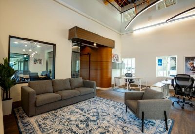 Lounge area with a grey sofa and patterned rug located next to a private glass office.