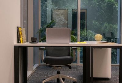 Private office workstation with a laptop and view of lush greenery through floor-to-ceiling windows.