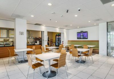 Bright communal dining area with white tables, wooden chairs, and a kitchen service window.