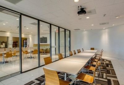 Long conference room with a white table, wooden chairs, and a glass wall looking into the cafe.