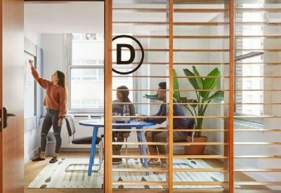 A modern meeting room with glass walls, wooden slats, and people working around a blue table.