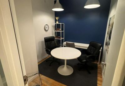 Private office featuring a white pedestal table, black leather chairs, and warm wood flooring.