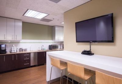 Bright communal kitchen area with dark cabinetry, a long white breakfast bar, and a wall-mounted TV.