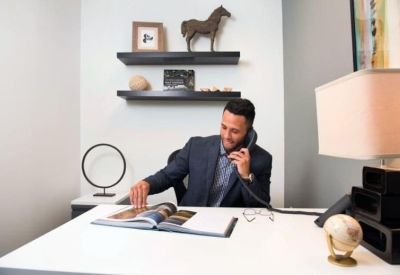 Professional private office with decorative wall shelving and a man at a white desk.