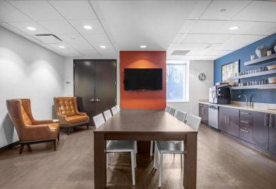 Modern breakout area with a long dining table, orange feature wall, and kitchen facilities.