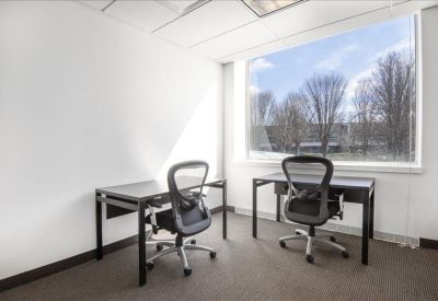 Bright private office with two desks and a large window overlooking trees.