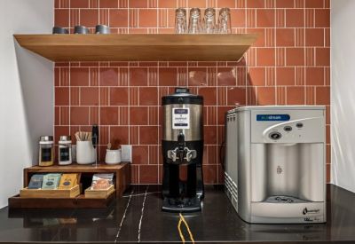 Self-service coffee and tea station with a red tiled backsplash and sleek black countertop.