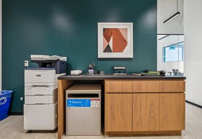 Printing and mail station against a dark teal wall featuring a wooden cabinet and abstract art.