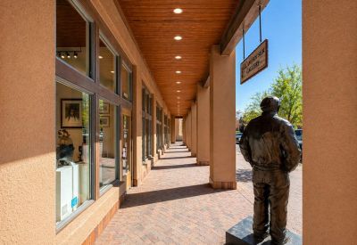 Outdoor pedestrian walkway with stucco pillars, a wooden ceiling, and bronze statues.