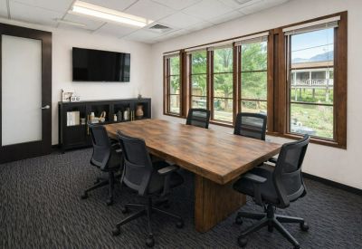 Six-person meeting room with a rustic wood table, dark patterned carpet, and large windows.