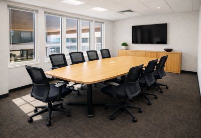 Spacious boardroom with a light wood table, black mesh chairs, and a wall-mounted television.