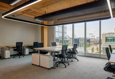 Bright open-plan workspace with multiple desks and floor-to-ceiling windows.