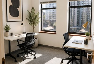 Two-person private office with white desks, ergonomic chairs, and city views through large windows.