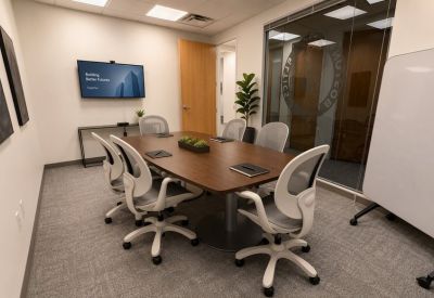 Modern meeting room with a dark wood table, grey chairs, and a wall-mounted TV screen.