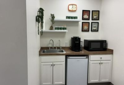A well-equipped communal kitchenette with a coffee machine, microwave, and white cabinetry.