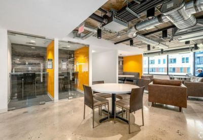 Bright coworking area with round tables, leather armchairs, and private glass phone booths.