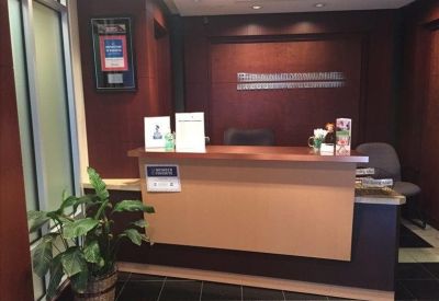 Modern wooden reception desk with a dark feature wall and potted plant.