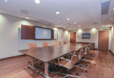 Professional boardroom with a long wooden table, tan chairs, and a presentation screen.