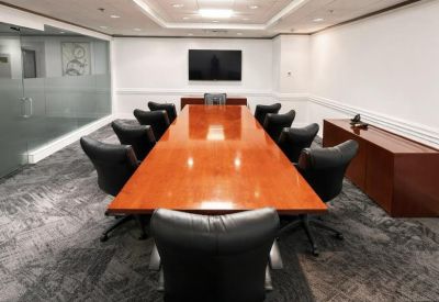 Conference room with a long polished wooden table and black leather chairs.