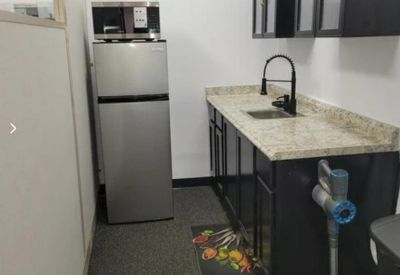 Functional kitchenette area with a stainless steel refrigerator and dark cabinetry.
