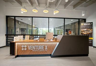 Modern reception desk with wooden paneling and Venture X branding under pendant lighting.