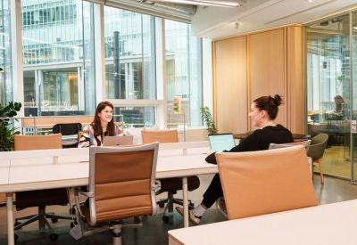 Open-plan coworking space with modern white desks and large windows overlooking the city.