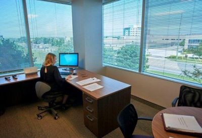 Private office suite featuring an L-shaped desk and large windows with blinds.