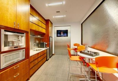 Modern communal kitchen and breakout area with wood cabinets, high-top orange seating, and a water feature.