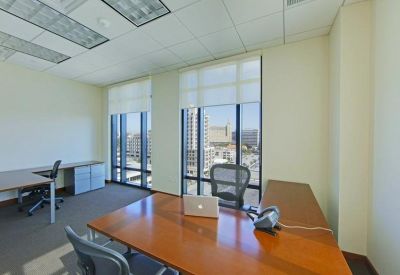 Private office suite with a large wooden desk, ergonomic chairs, and city views through large windows.
