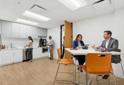 Modern communal kitchen and break area with white cabinetry and orange bar stools.