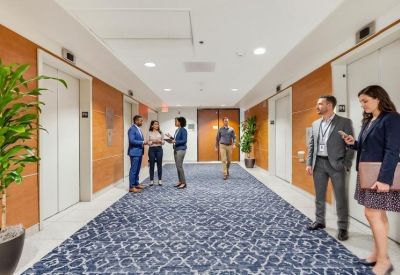 Bright elevator lobby featuring patterned blue carpet, wood-paneled walls, and indoor plants.