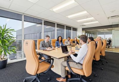 Spacious boardroom with a light wood table, tan leather chairs, and a large window.