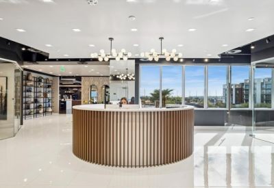 Bright reception area with a circular wood-slat desk and large windows.