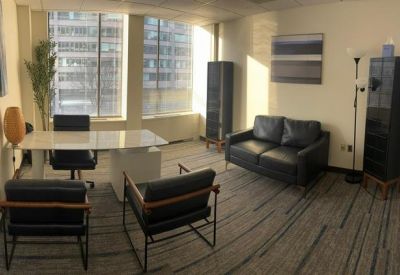Contemporary private office with a black leather sofa, white desk, and large city-view windows.