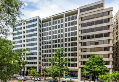 Street-level view of the office building showing mature green trees and urban surroundings.