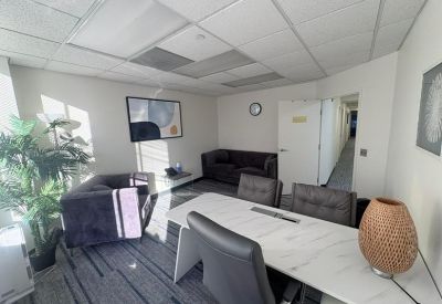 Brightly lit common area with a white conference table, grey sofas, and potted plants.